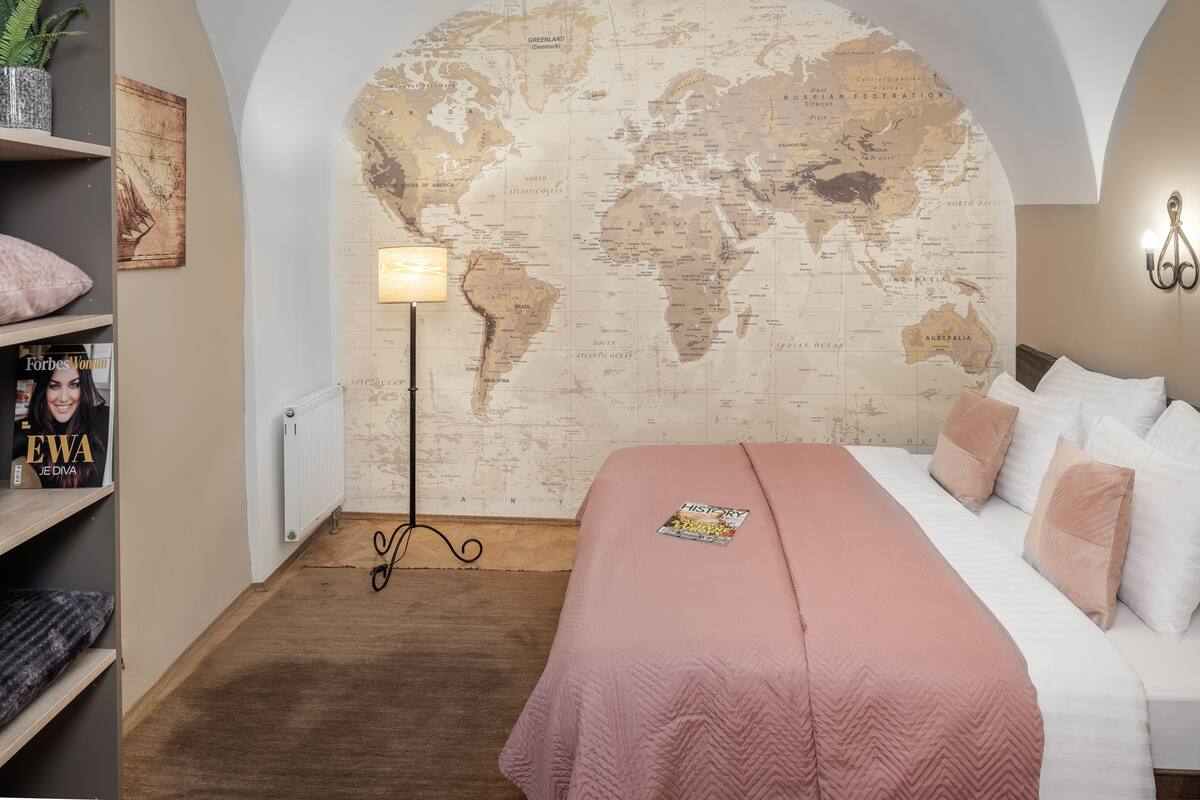 Ein Schlafzimmer mit Wandweltkarte, einer Stehlampe, einem Bücherregal mit einer Zeitschrift und einem Bett mit einer rosa Decke.