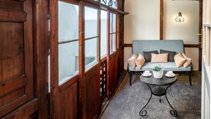 Una habitación acogedora con techo de madera, un sofá azul con cojines, una mesita redonda con taza y platillo, y una barandilla metálica decorativa.