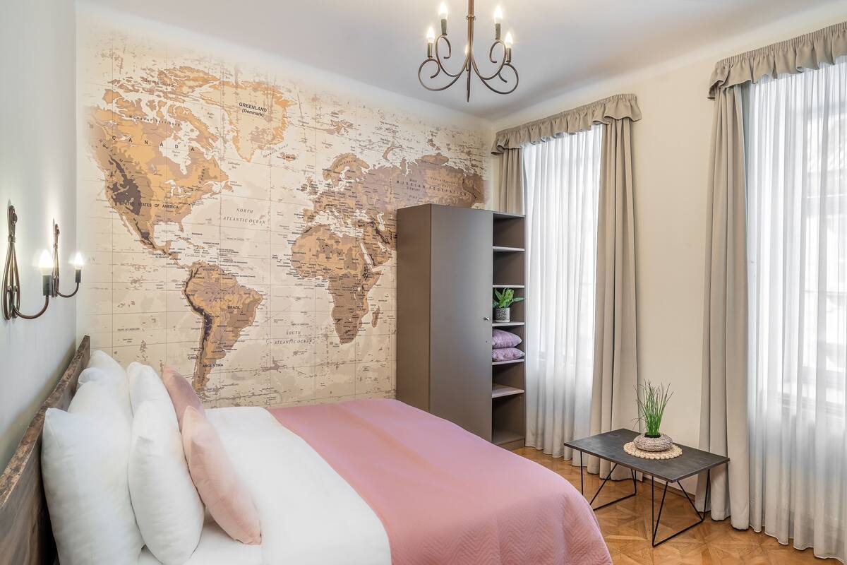 Ein Schlafzimmer mit Wandweltkarte, einem Bett mit Kissen, einem Kleiderschrank, einem kleinen Tisch mit Pflanze und einem Hängegestell mit Tasche.