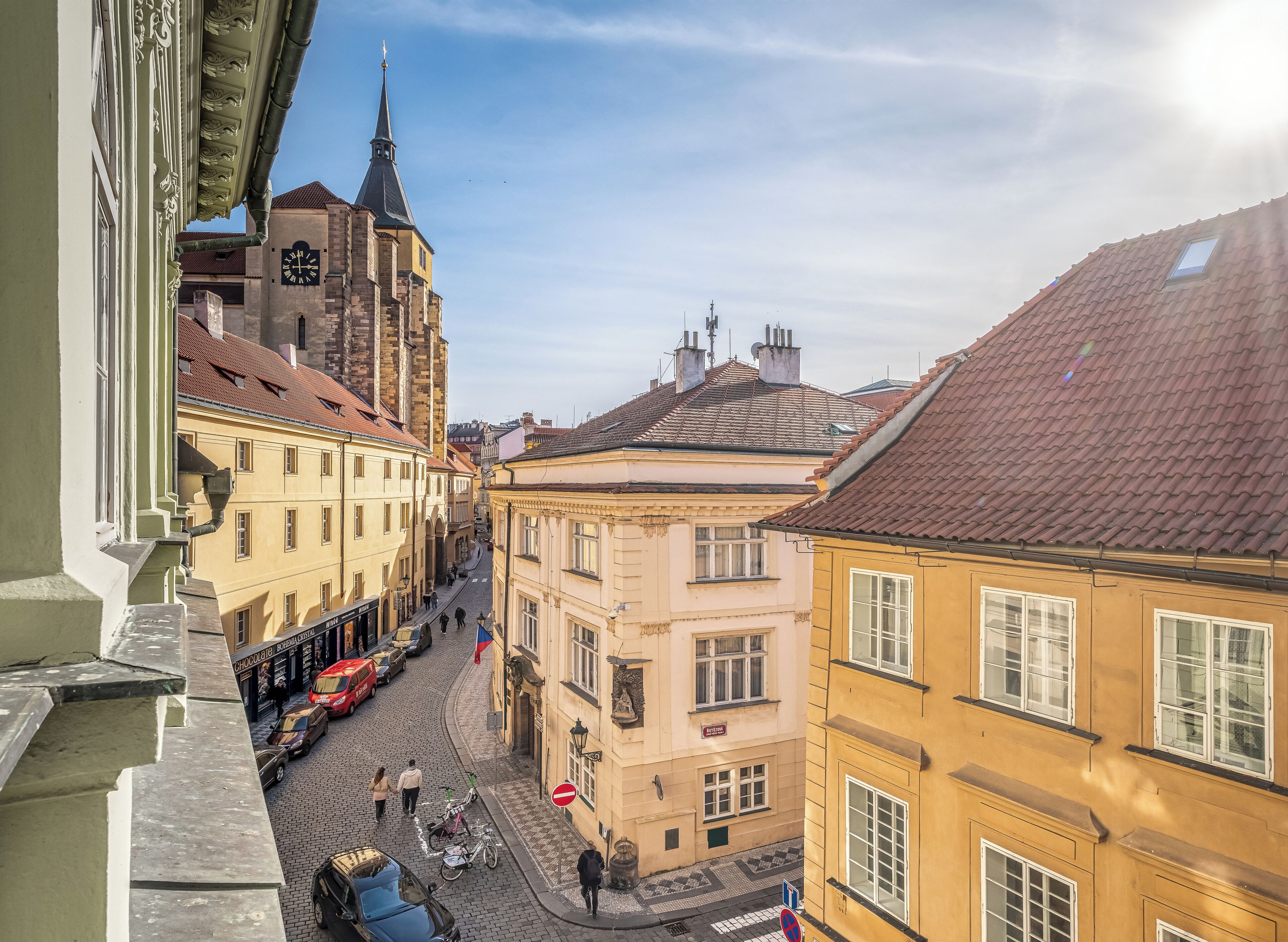 A cobblestone street with historic buildings, a church spire, and a tram.
