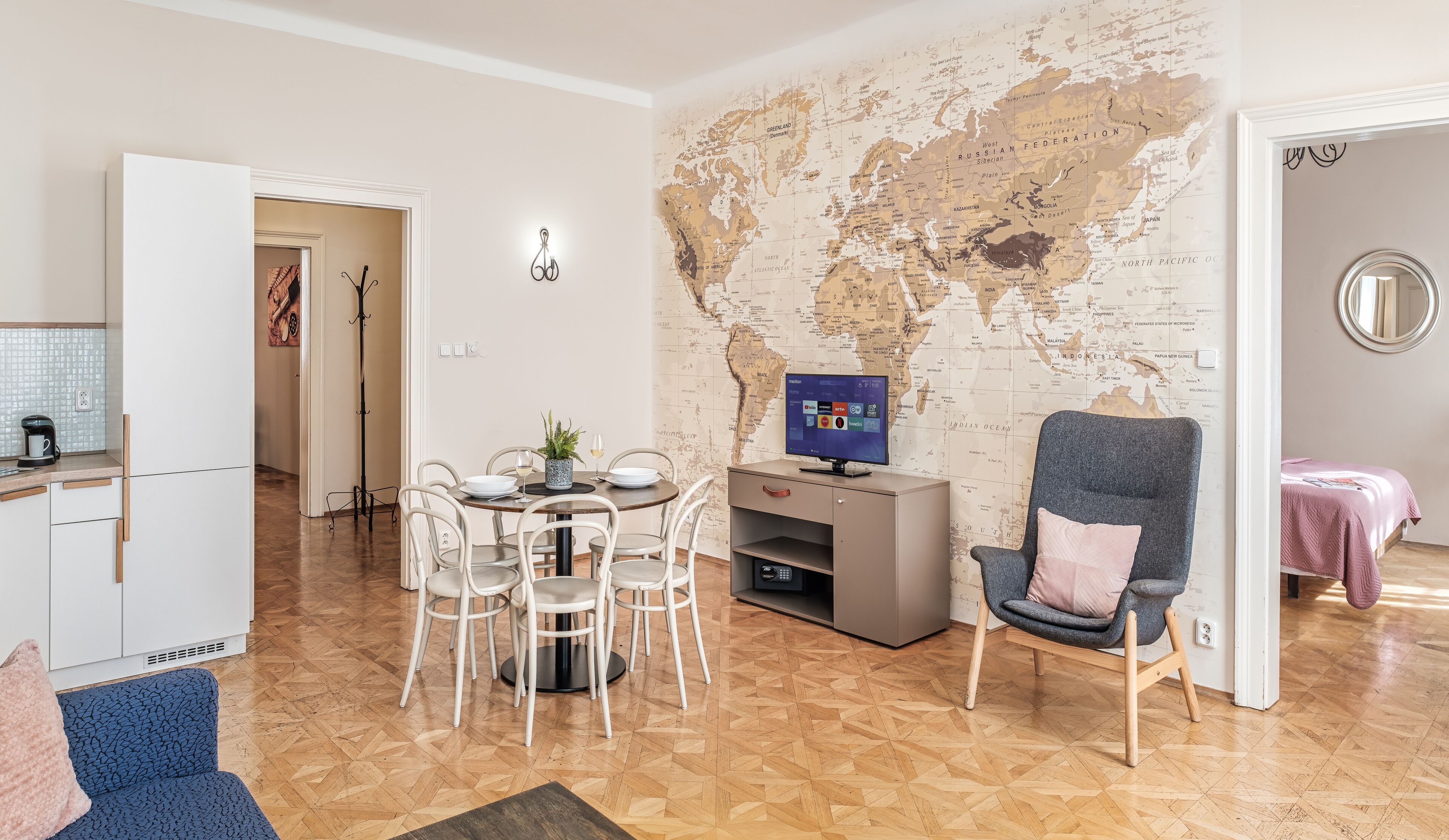 A modern living room with a world map wall, a dining area with white chairs, a grey armchair, and a TV.