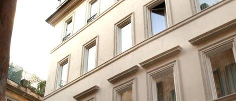 Un edificio de varios pisos con fachada beige, ventanas numeradas y una entrada central en arco.