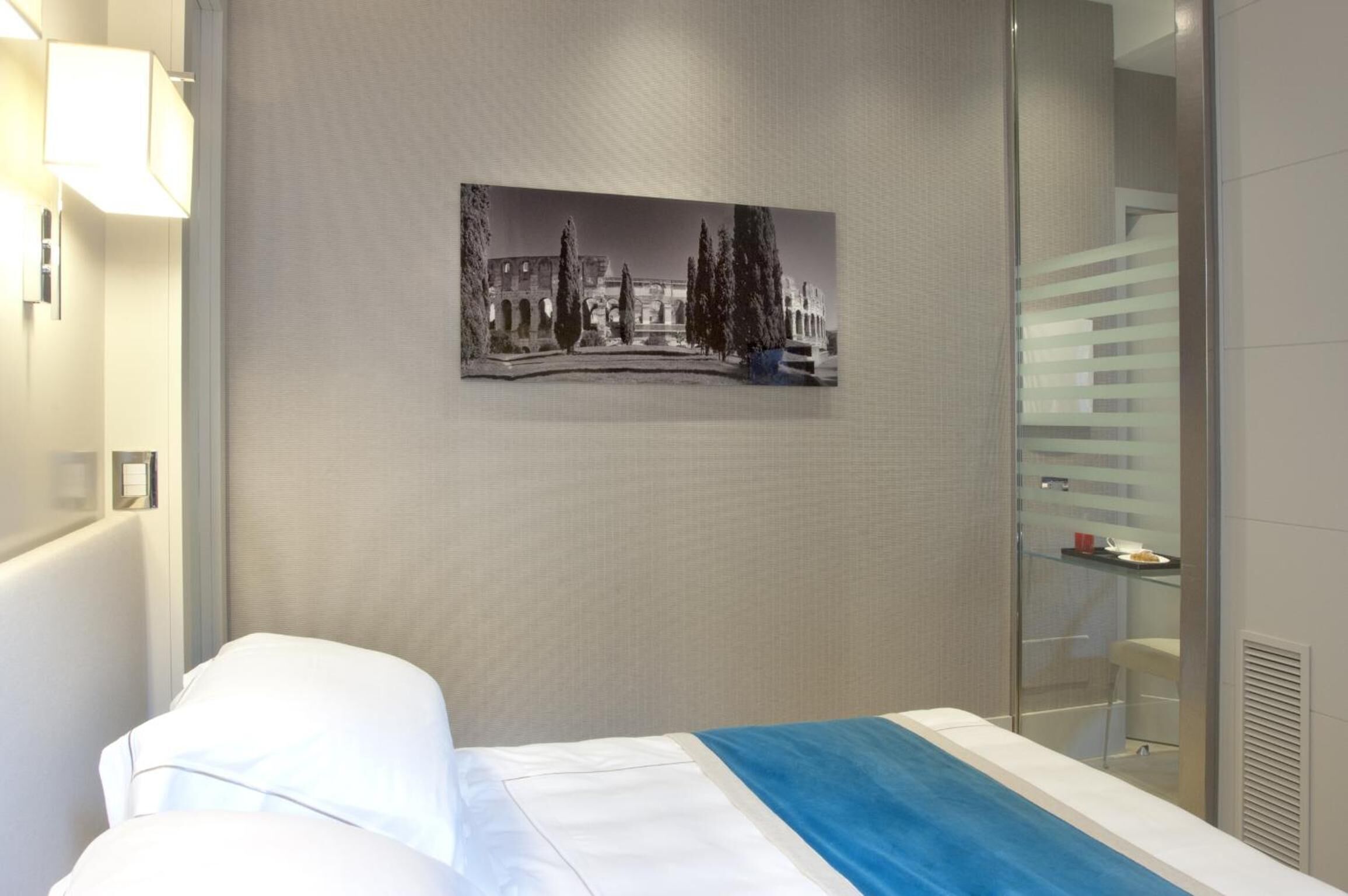 A hotel room with a bed, a wall-mounted picture, a glass shower enclosure, and a light fixture.