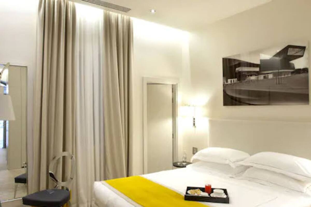 A hotel room with a bed, curtains, a bedside table, a lamp, and a framed picture on the wall.
