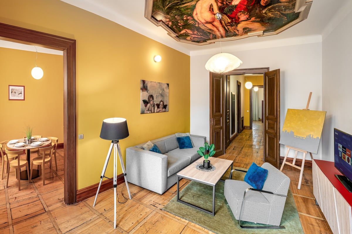 A living room with a dining table, sofa, and an easel with a painting.