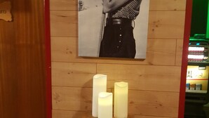 Een houten wand met een poster van een persoon die een camera vasthoudt, een houten tafel met drie kaarsen, en een rode deuropening.