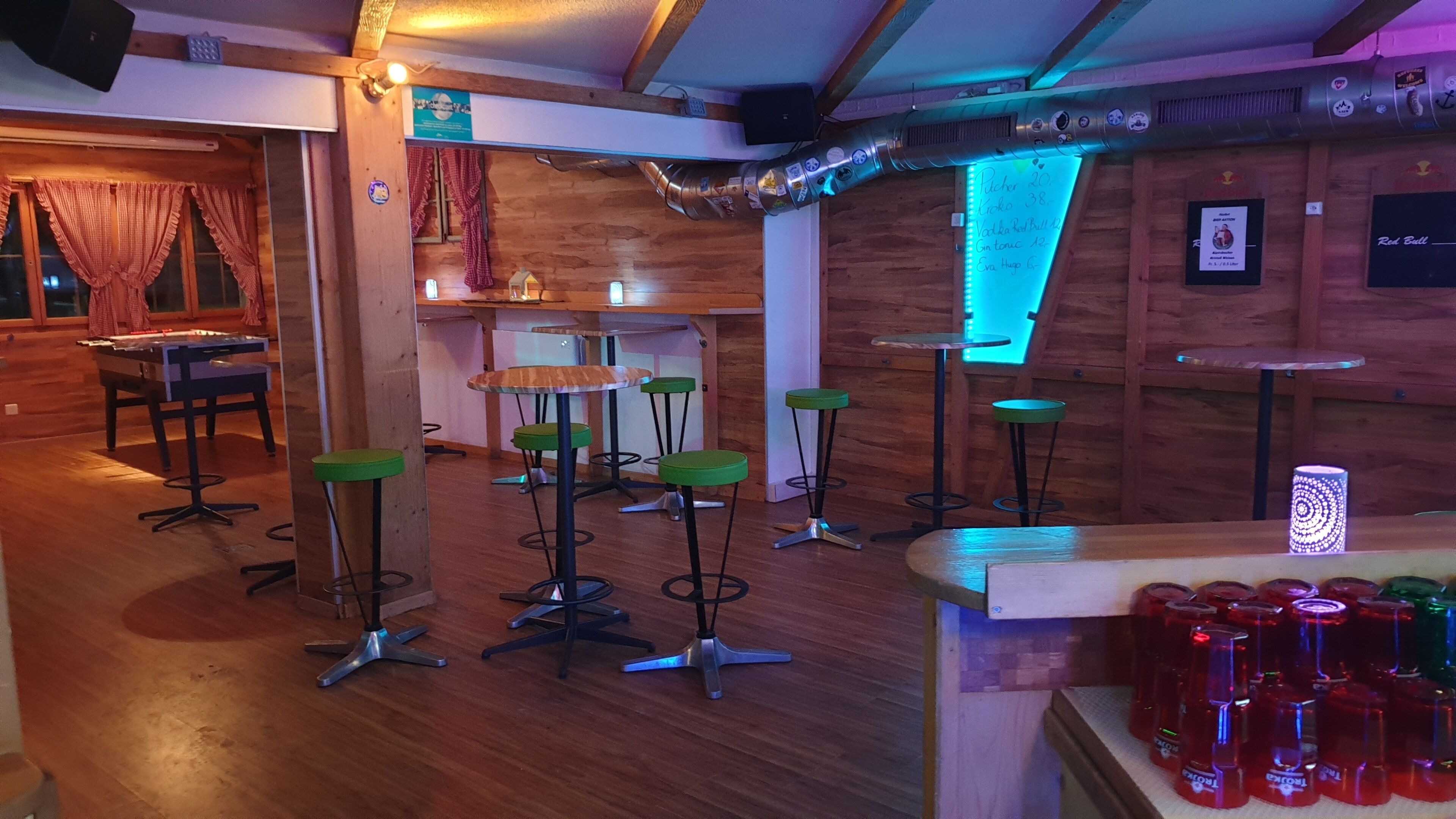 A bar area with wooden walls, green bar stools, and a variety of bottles on the counter.