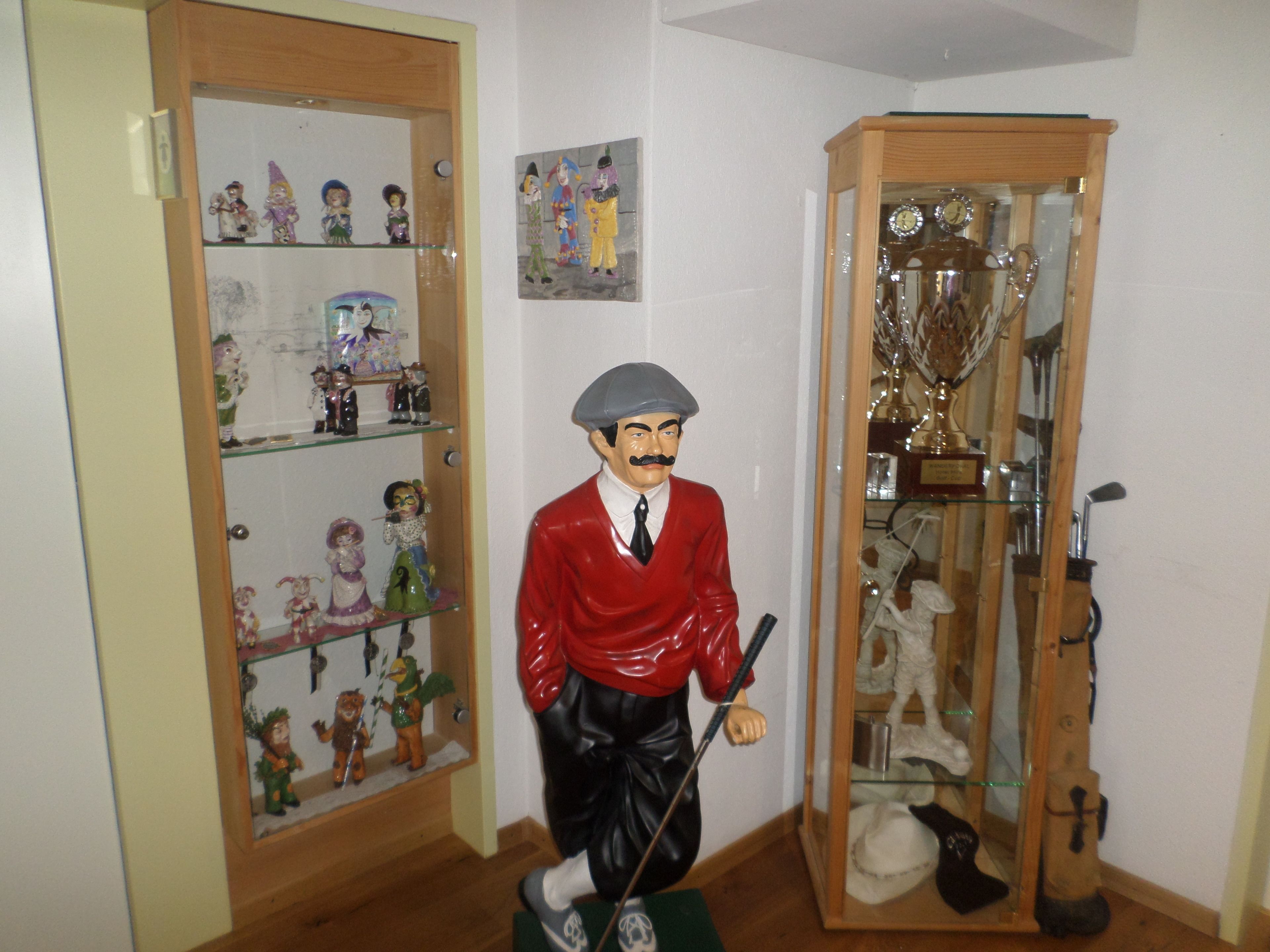 A room with a wooden door, a glass display cabinet with figurines, and a trophy cabinet.