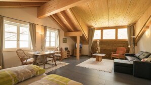 A cozy room with a wooden ceiling, a dining area with a table and chairs, a sofa, and a bed with green and white bedding.