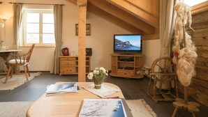 A cozy room with a wooden ceiling, a television, a spinning wheel, and a table with a vase of flowers.