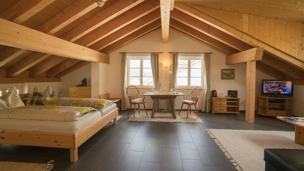 A spacious loft bedroom with a large bed, a dining table with chairs, and a TV in the corner.