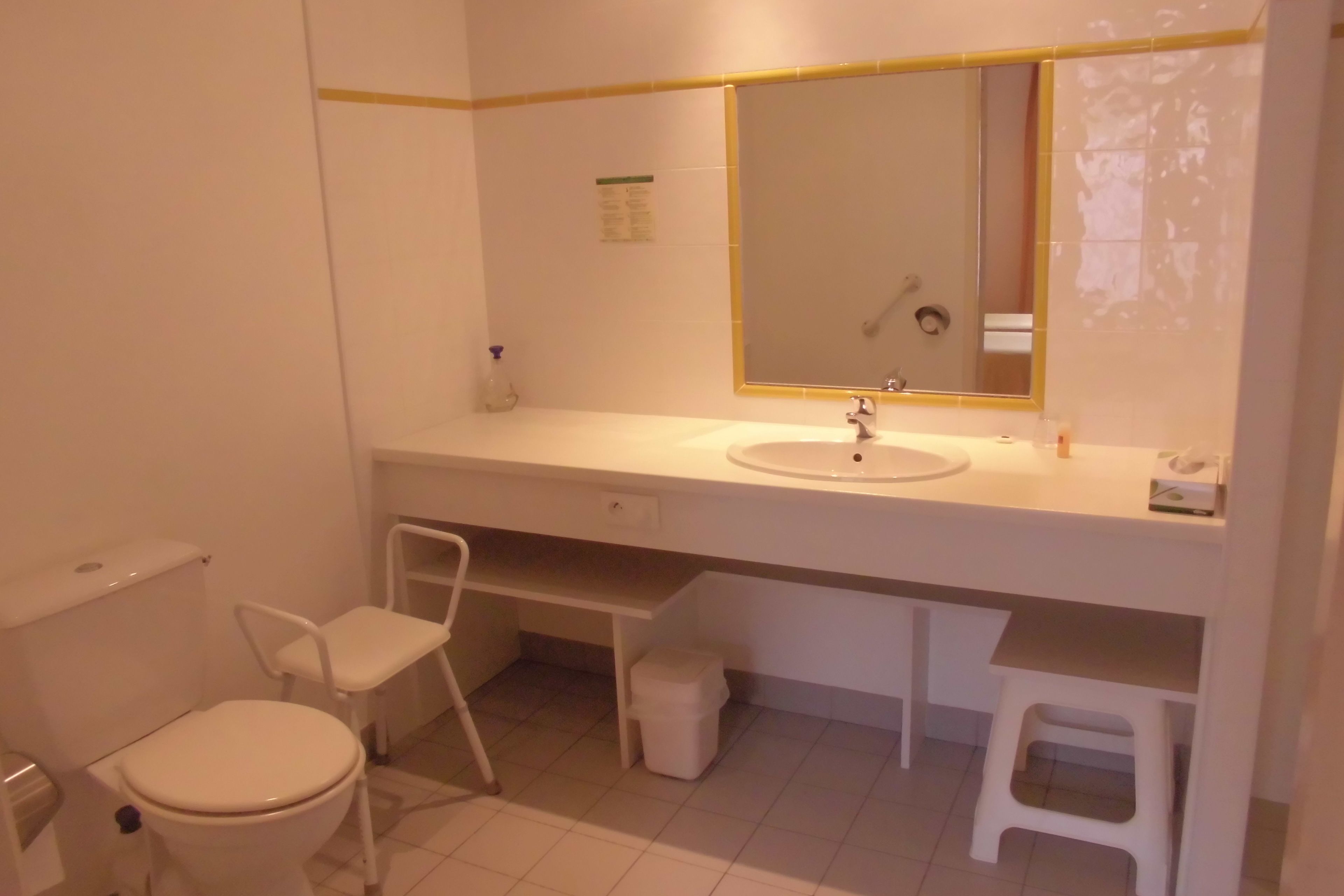 A bathroom with a toilet, a sink, a mirror, and a small stool.