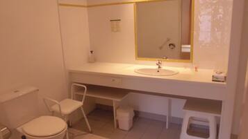 A bathroom with a toilet, a sink, a mirror, and a small stool.