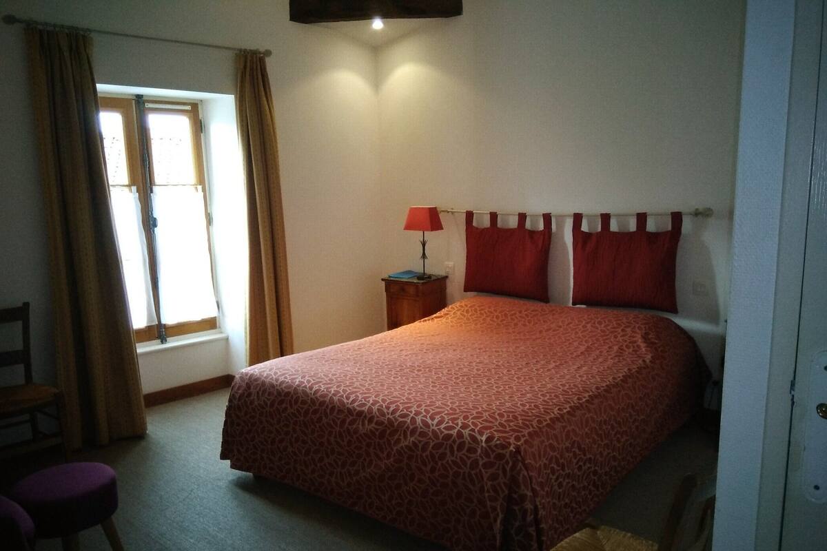 A bedroom with a large bed, a nightstand, a chair, and a window with curtains.