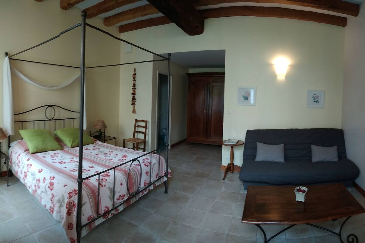 A bedroom with a four-poster bed, a sofa, a small table, and a TV.