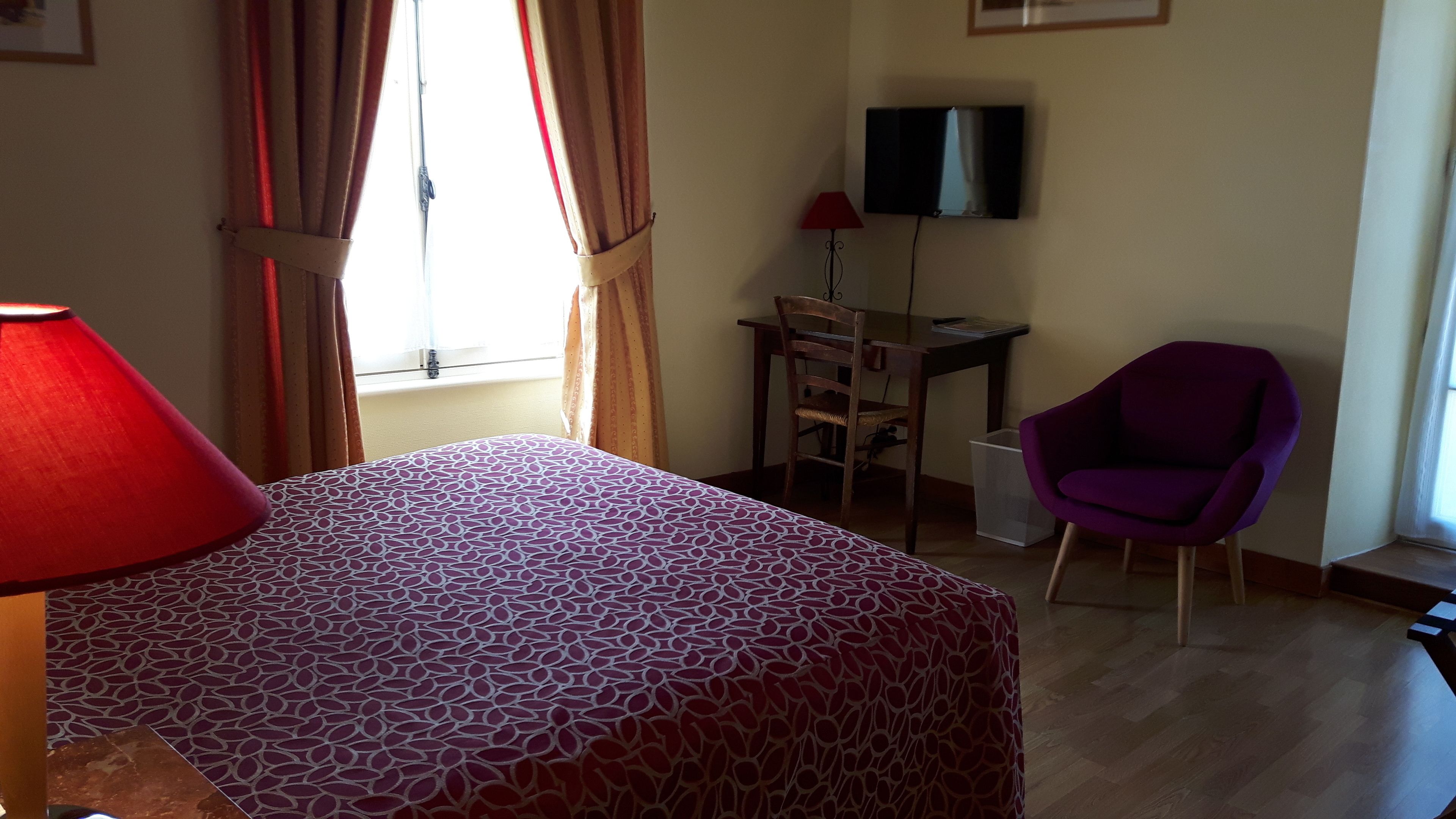A hotel room with a bed, a desk, a chair, a TV, and a window with curtains.