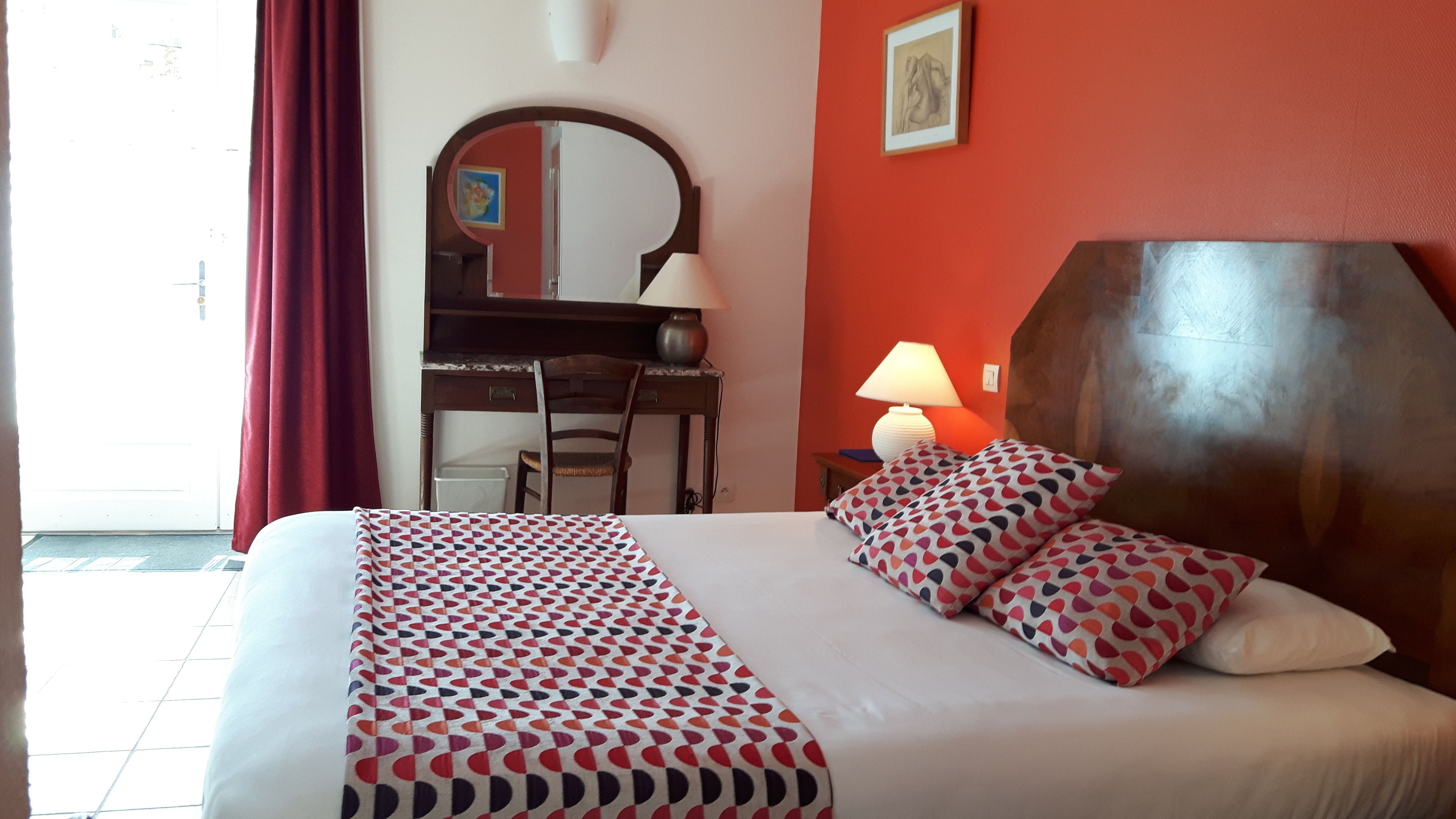 A hotel room with a bed, a desk, a chair, a lamp, and a large mirror.
