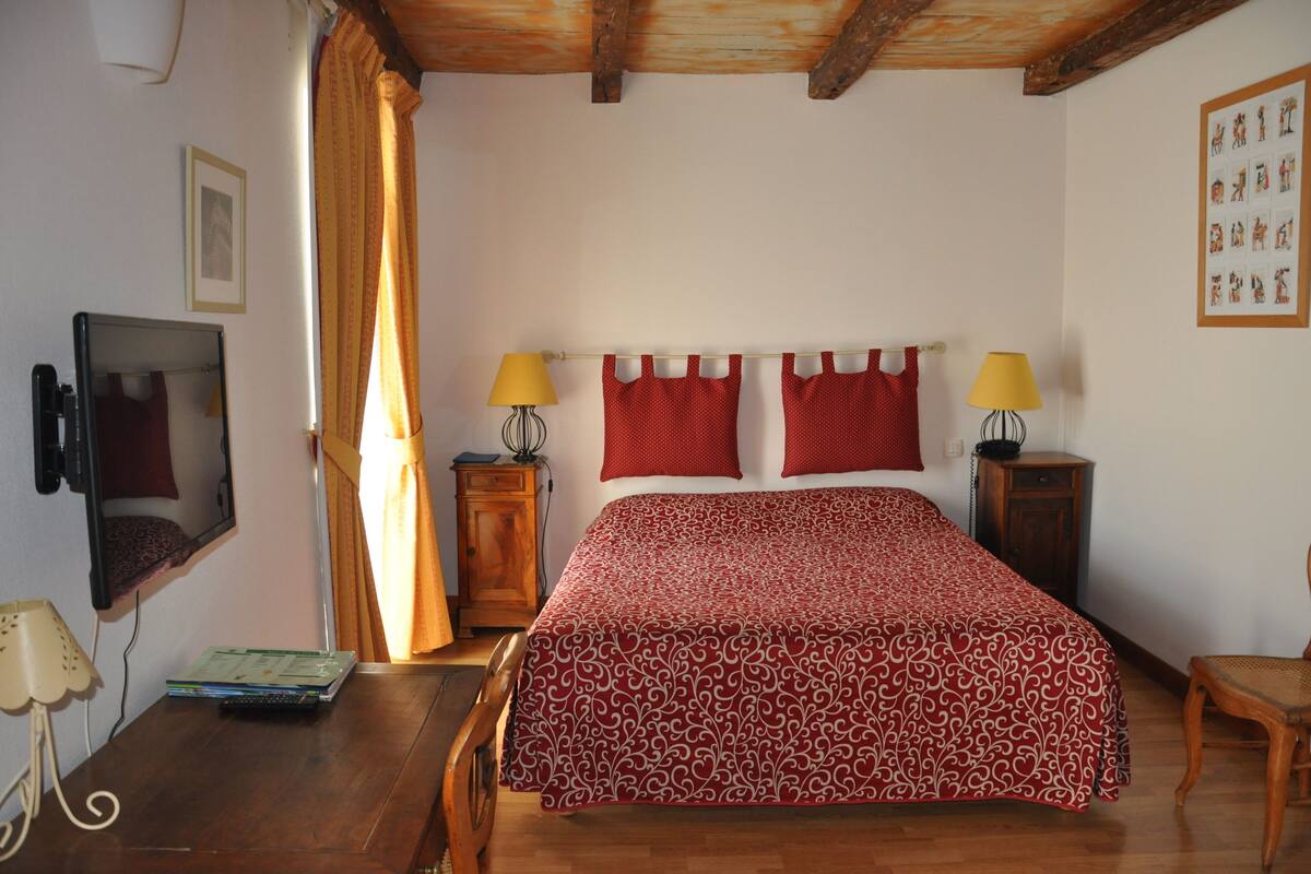 A bedroom with a bed, two bedside lamps, a TV, a wooden cabinet, and a chair.