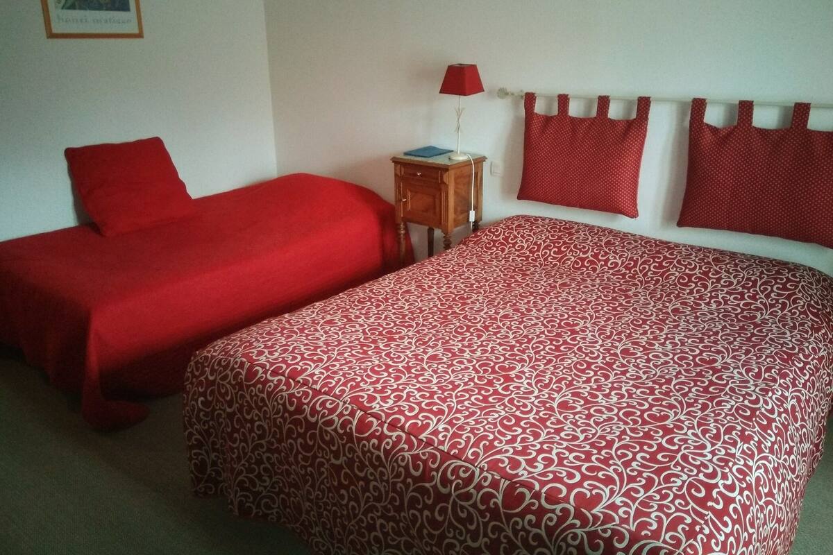 A room with two beds, a small wooden nightstand with a lamp, and a framed picture on the wall.