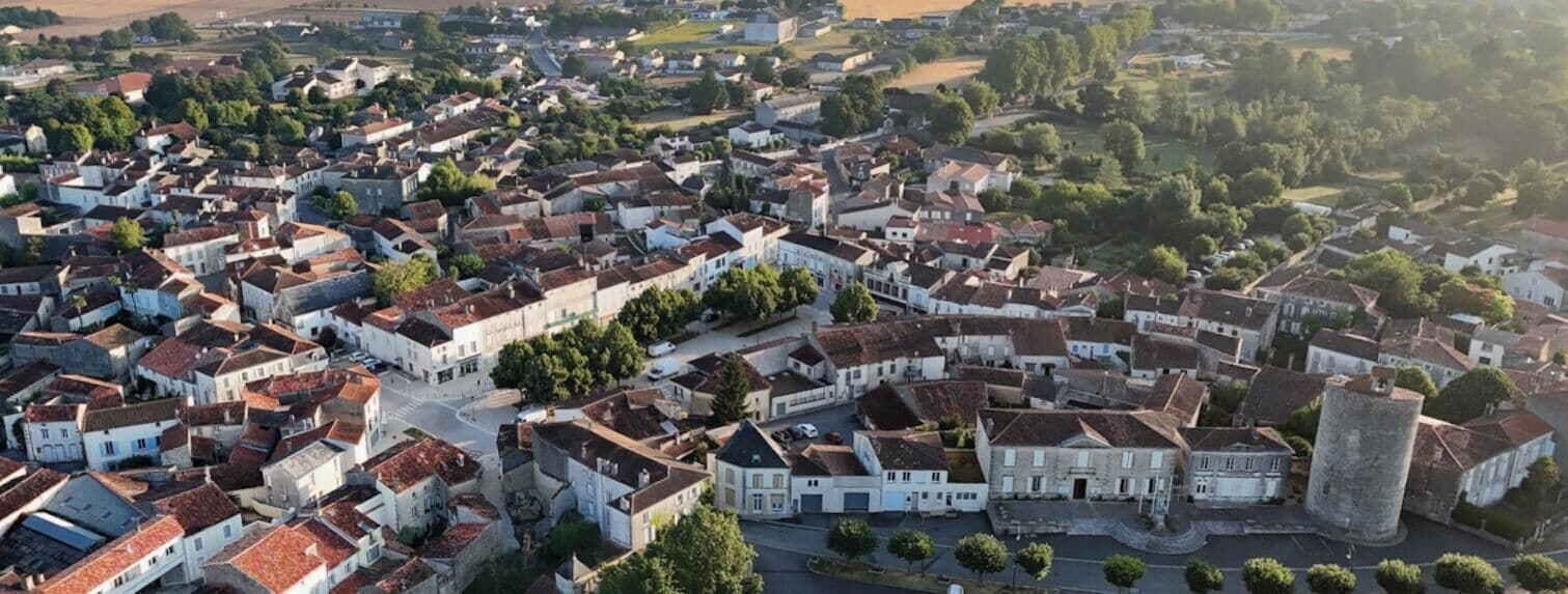 An aerial view of a historic town with tightly packed buildings, a prominent tower, and a central square.