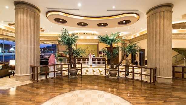 Een hotel lobby met een receptiebalie, palmbomen en een incheckruimte.