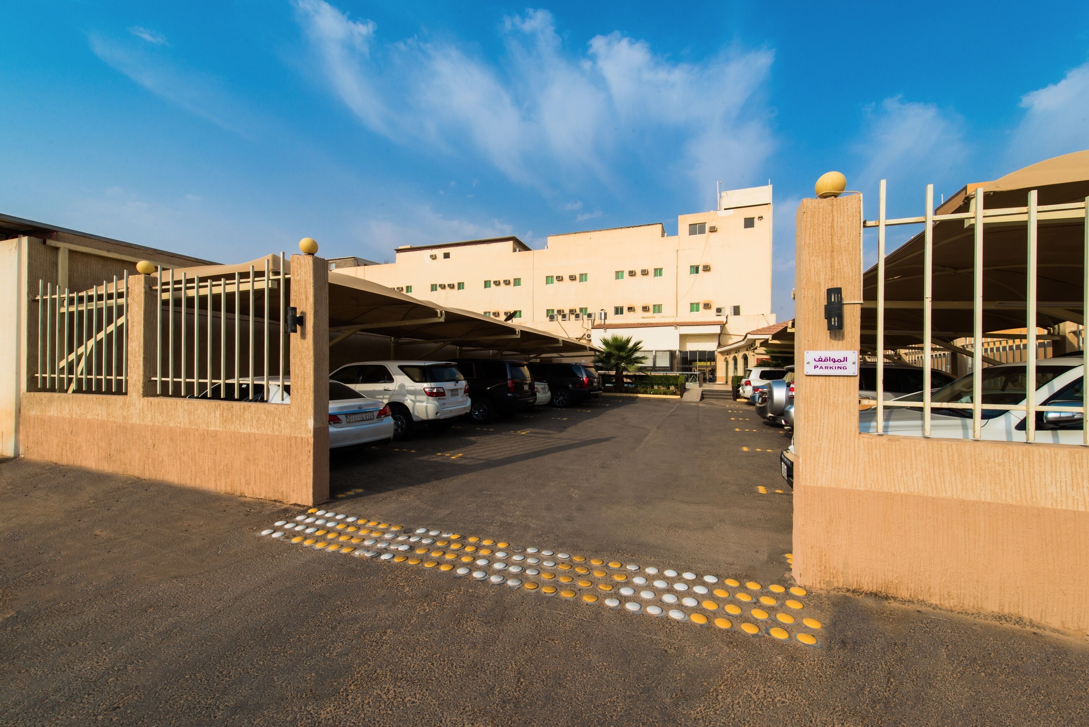 A parking area with cars, a building with multiple windows, and a clear sky.