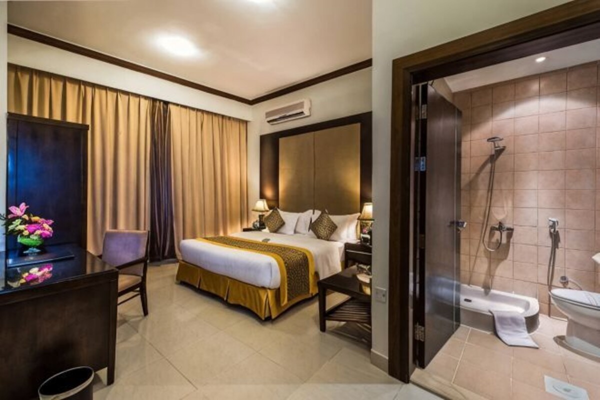 A hotel room with a bed, desk, chair, and a shower area.