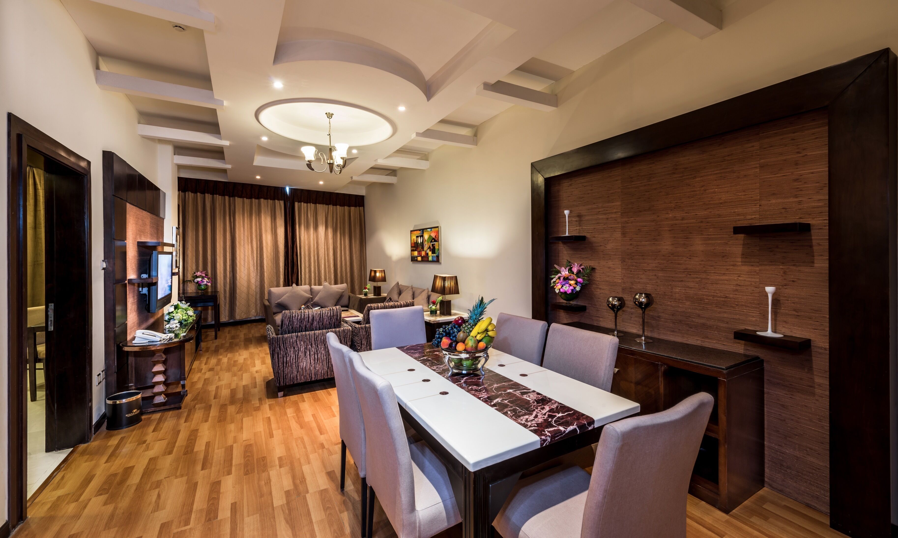 A modern dining area with a marble table, cushioned chairs, a chandelier, and a wooden accent wall.