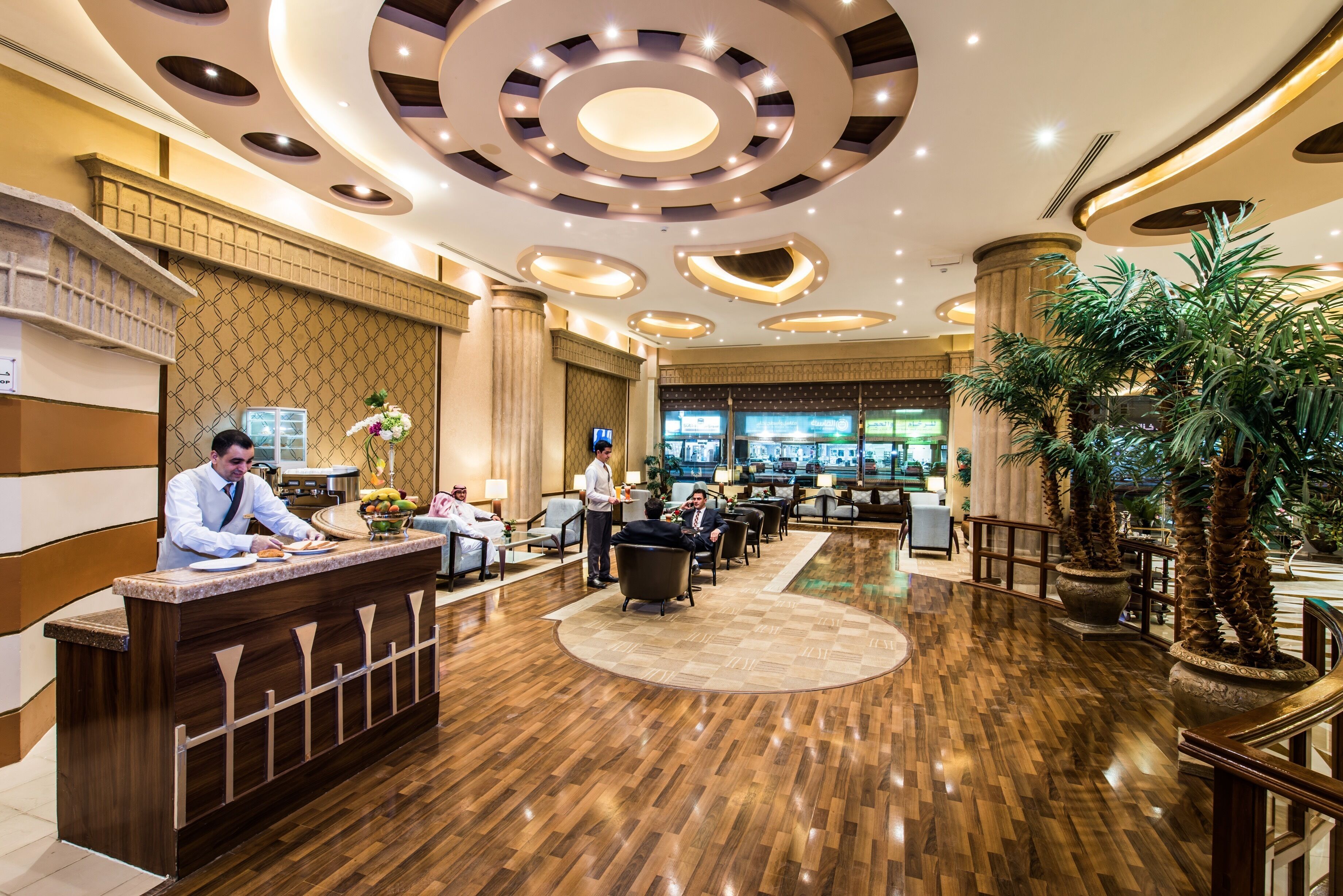 A hotel lobby with a reception desk, seating area, and large windows.