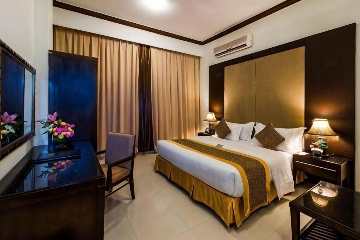 Una habitación de hotel con cama, mesitas de noche, escritorio, silla y espejo.