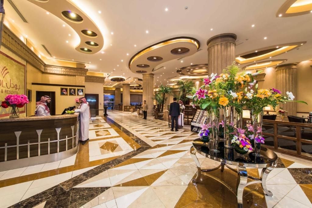 Un vestíbulo de hotel con una recepción, un mostrador de check-in y un área de descanso con un arreglo floral.