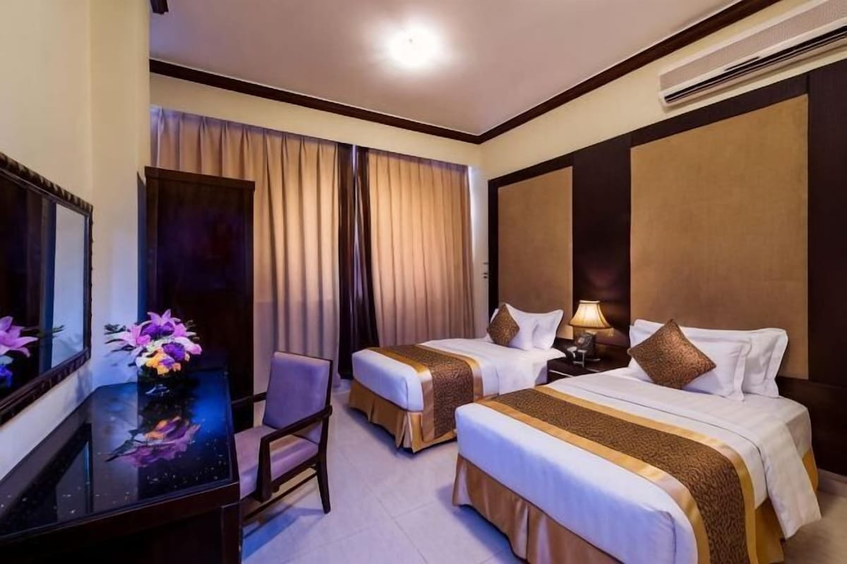 Habitación de hotel con dos camas, un escritorio con silla, un espejo y una ventana con cortinas.