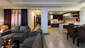 A modern hotel room with a living area featuring a sofa, a coffee table, and a lamp. The room includes a kitchen area with a dining table and chairs. - Boudl Rass (Ar Rass)