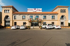 A hotel with a sign reading "BOUDL AL BASS" and a parking lot with several white cars.