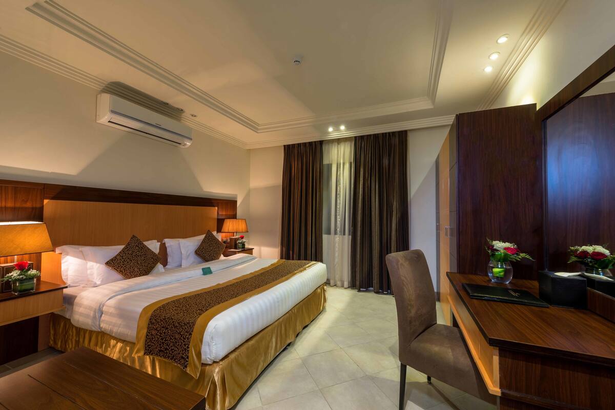 Habitación de hotel con una cama grande, un escritorio, una silla, un equipo de aire acondicionado y una ventana con cortinas.