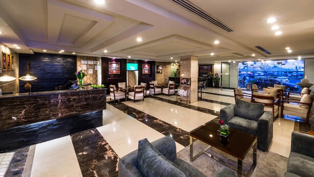 A hotel lobby with a reception desk, seating area, and a view of the cityscape through large windows. - Boudl Rass (Ar Rass)