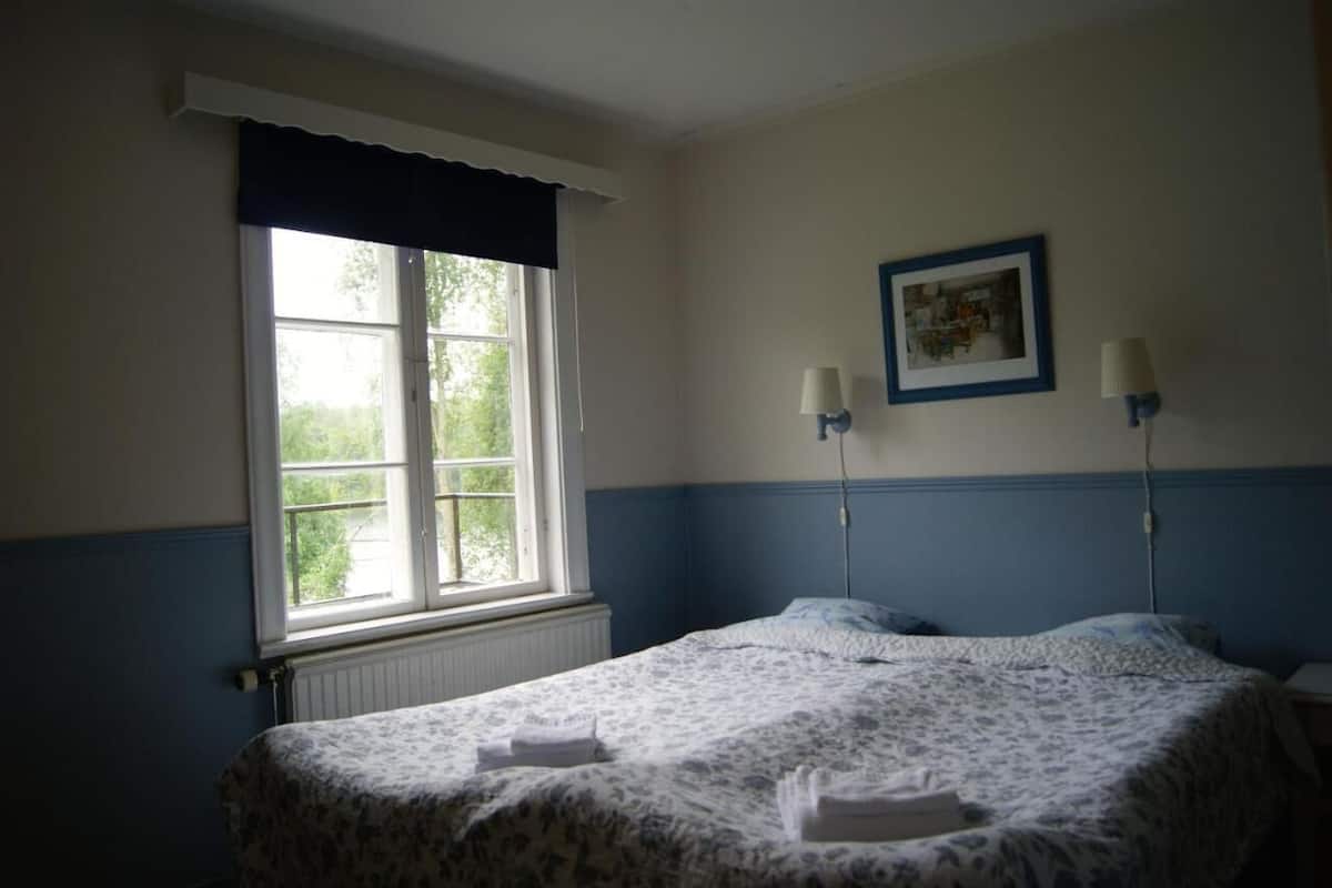Un dormitorio con cama, ventana con vista a zonas verdes y dos lámparas de pared.