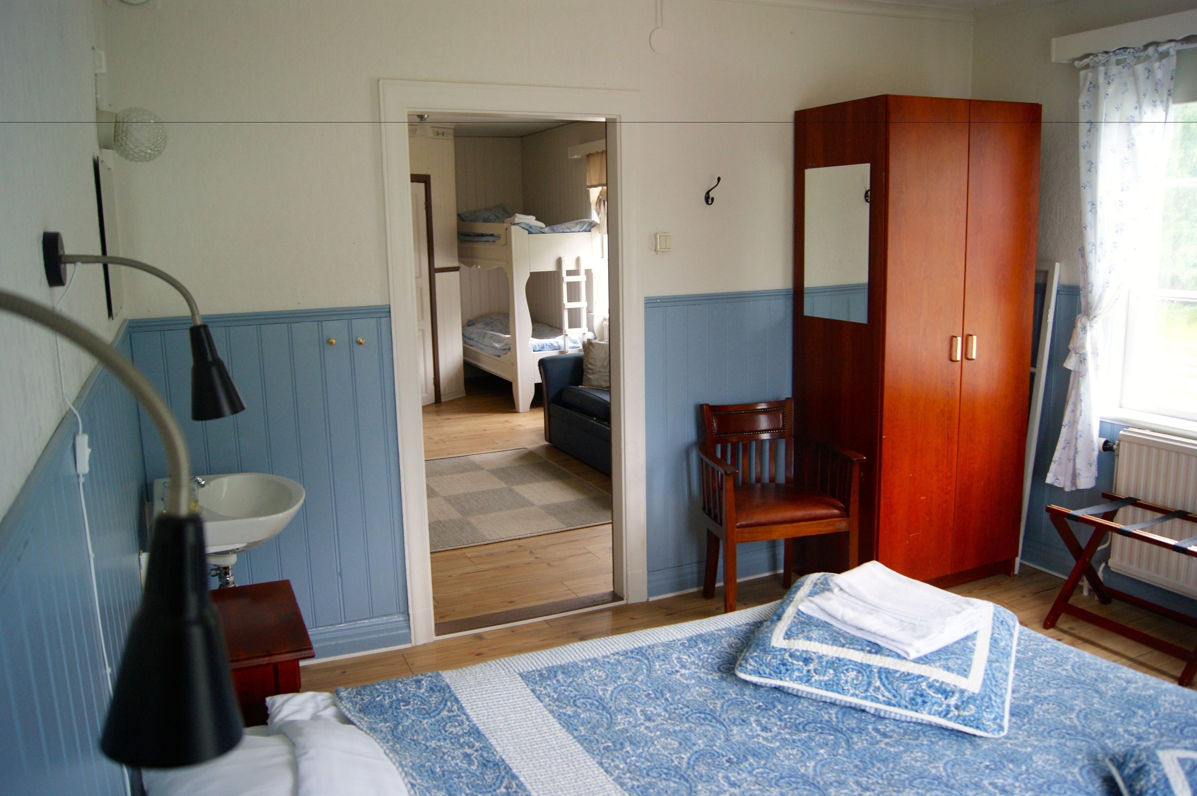 Een slaapkamer met een stapelbed, een houten garderobe, een nachtkastje, een lamp en een raam met gordijnen.