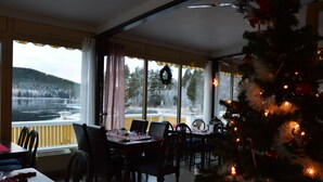 A dining area with a view of a lake, a Christmas tree, and a wreath on the windowsill. - Lugnet Malung Hotel (Malung)