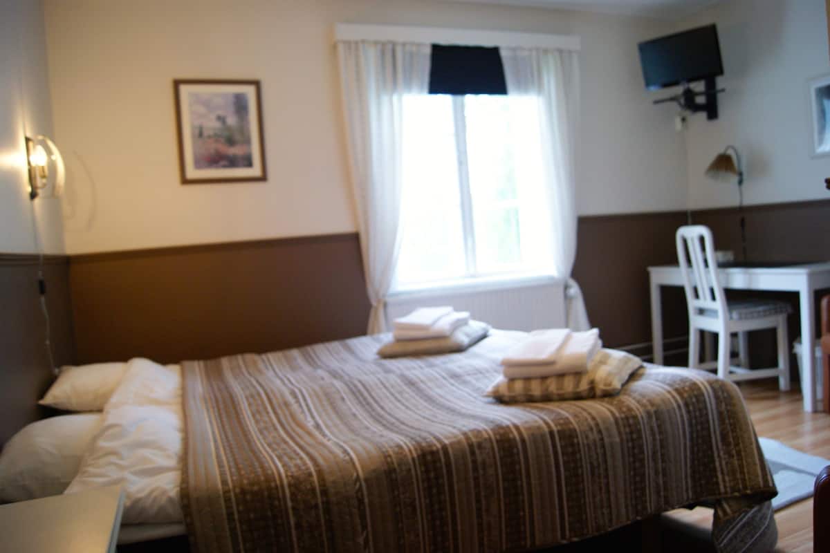 Una habitación de hotel con una cama, un escritorio, una silla y un televisor en la pared.