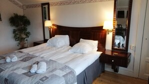 A neatly made bed with pillows and rolled towels, a bedside lamp, a mirror, and a potted plant in a hotel room. - Lugnet Malung Hotel (Malung)