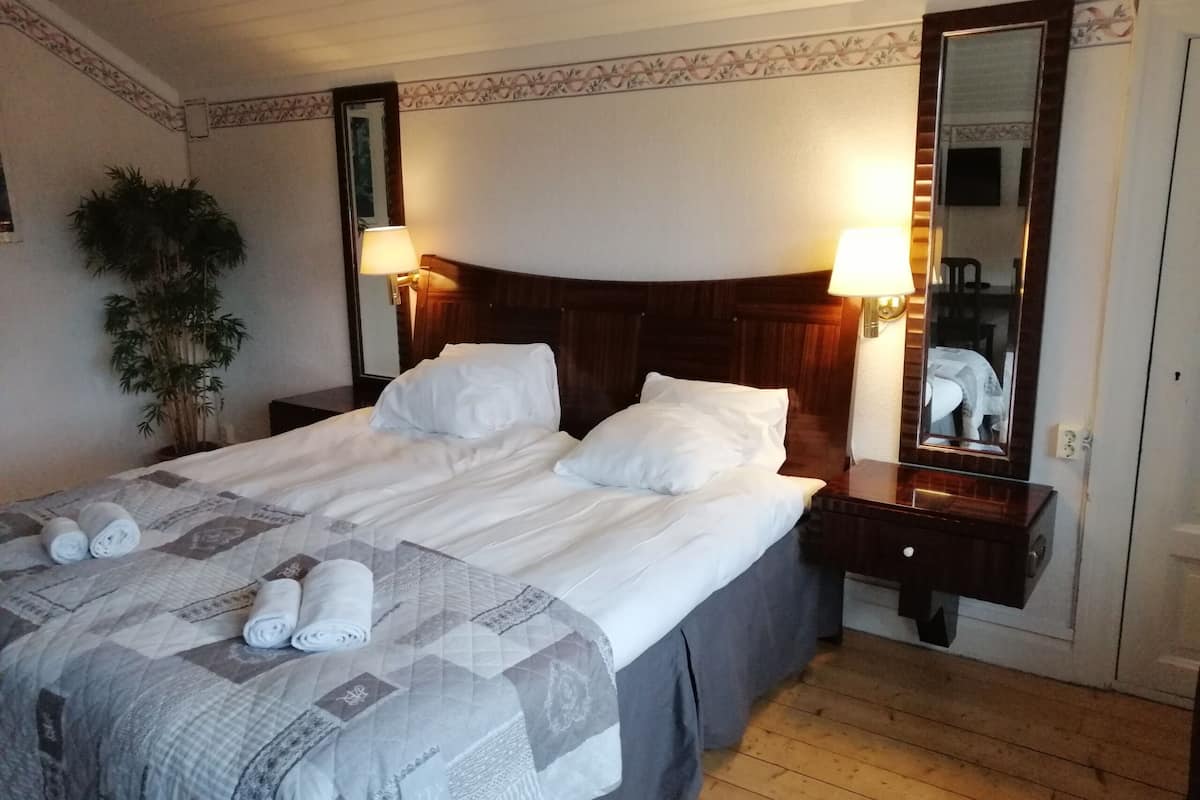 Una cama bien hecha con almohadas y toallas enrolladas, una lámpara de noche, un espejo y una planta en maceta en una habitación de hotel.