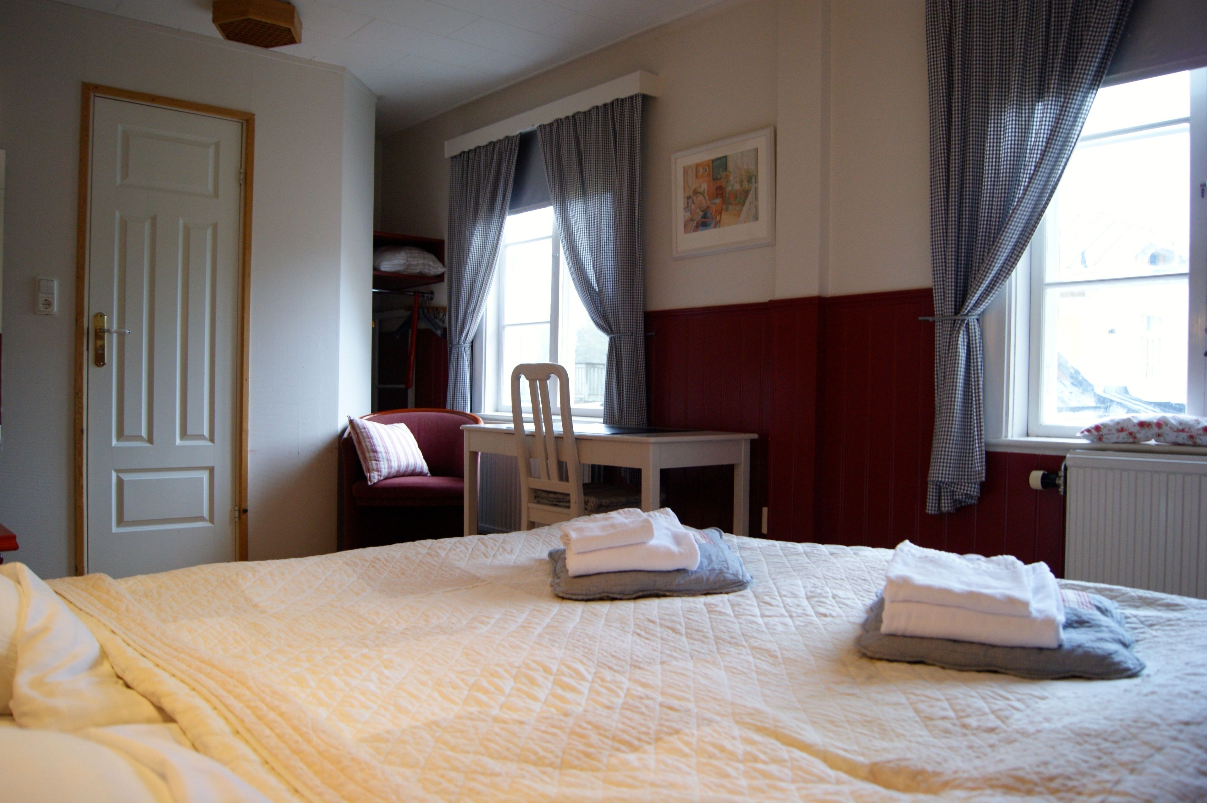 A hotel room with a bed, a chair, a table, and a window with curtains.