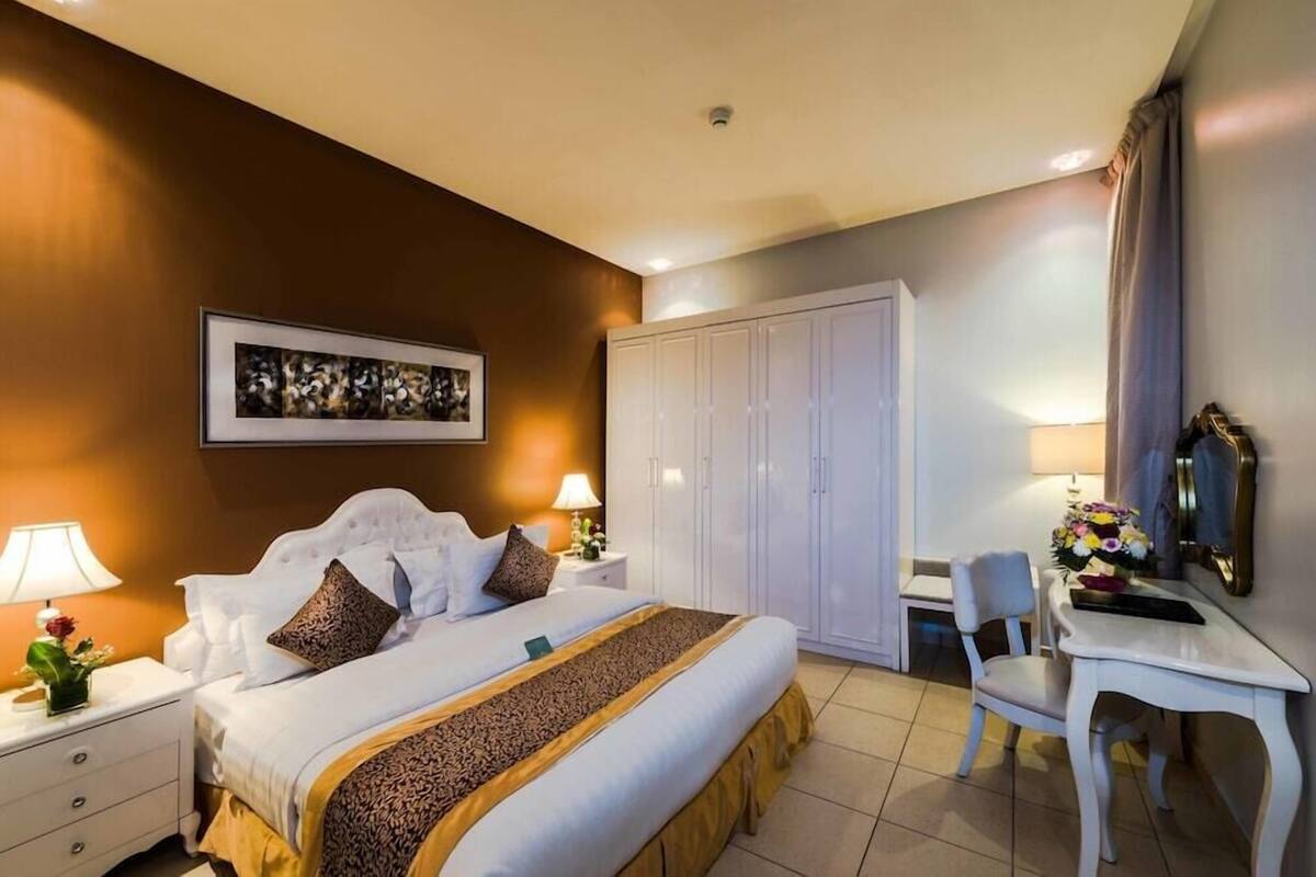 Une chambre d’hôtel comprenant un lit, des tables de chevet, un bureau, une chaise, une armoire et un tableau encadré au mur.