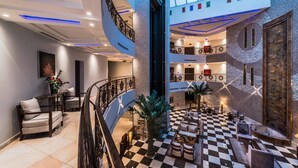 A spacious lobby with a checkered floor, a central palm tree, and a staircase leading to upper levels. - Boudl Al Fakhria (Unaizah)