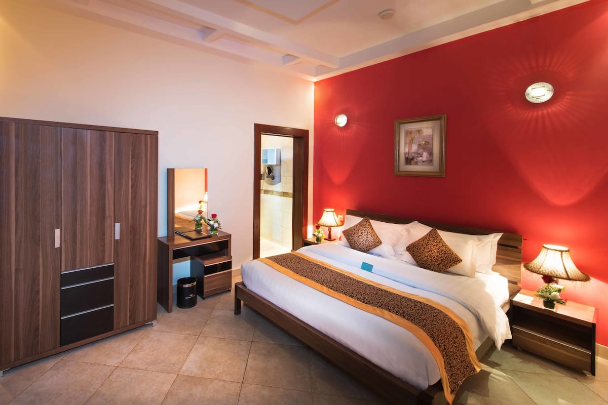 Quarto de hotel com cama, guarda-roupa, escrivaninha e mesa de cabeceira.