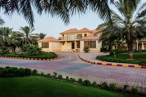 A two-story building with a tiled roof, surrounded by palm trees and a landscaped garden. - Boudl Nakhil  (Unaizah)