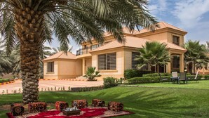 A large, two-story house with a tiled roof, surrounded by a well-maintained lawn and palm trees. - Boudl Nakhil  (Unaizah)