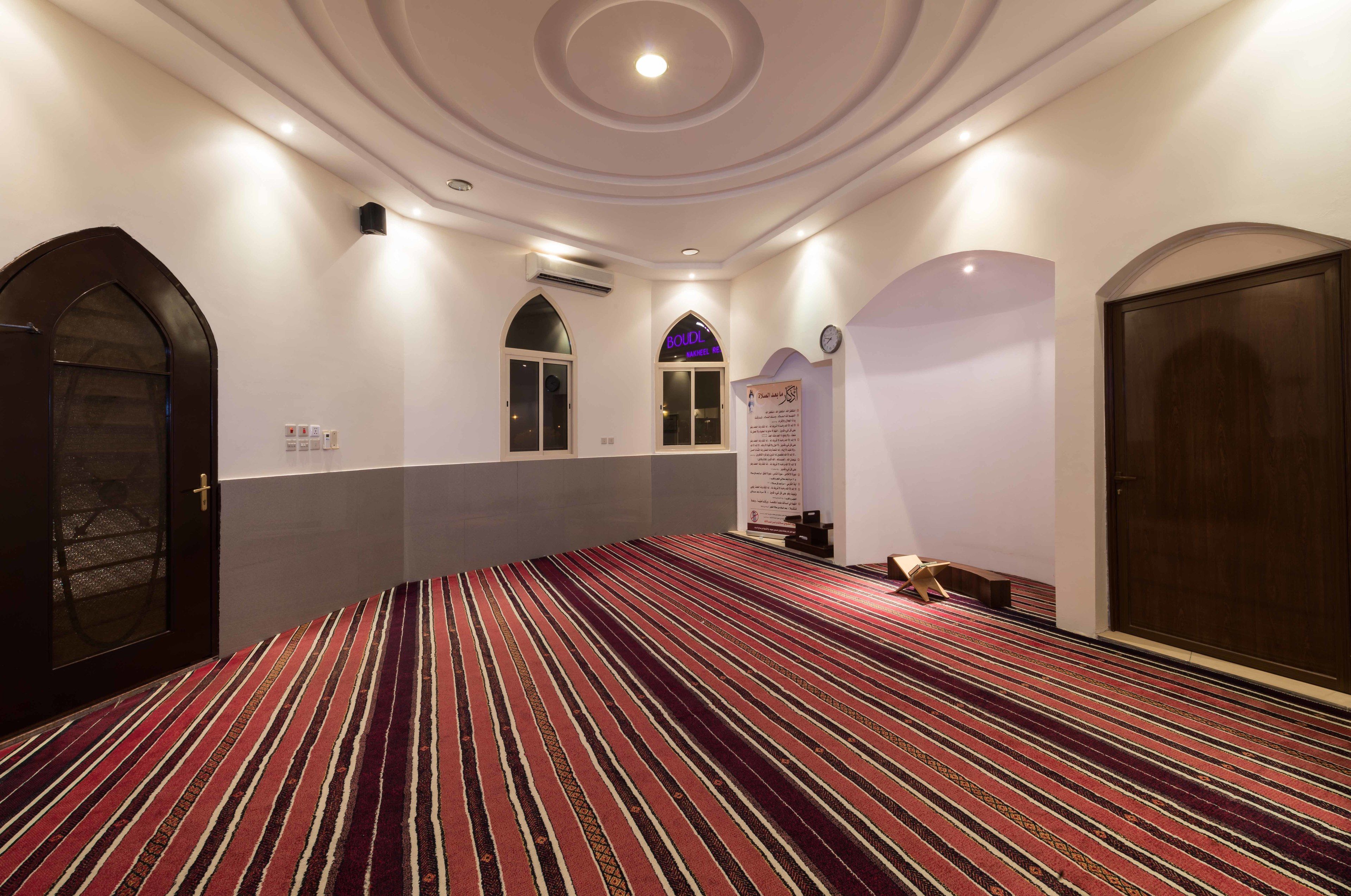 A hotel room with a striped carpet, a large arched doorway, a clock on the wall, and a sign above the door.