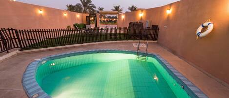 A swimming pool with a tiled edge, surrounded by a low fence and a wall with lights.